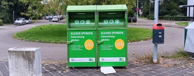Zwei Altkleider-Sammelcontainer in Mannheim, daneben hängt ein öffentlicher Mülleimer.